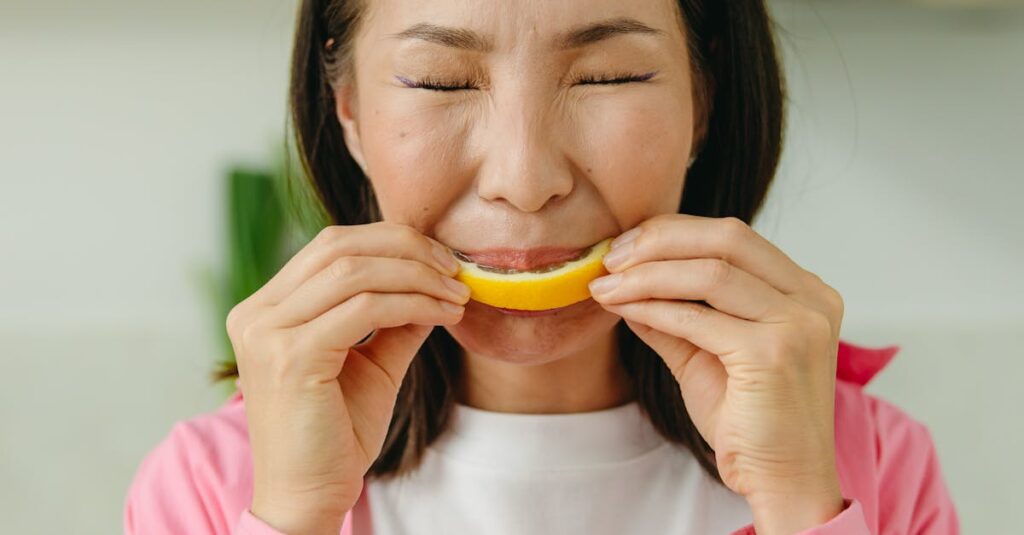 Asian woman in pink shirt makes a funny face while tasting a sour lemon slice indoors.
