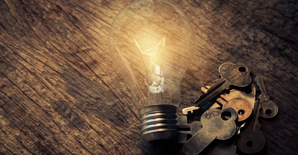 Illuminated vintage light bulb beside keys on rustic wooden table, symbolic of ideas.